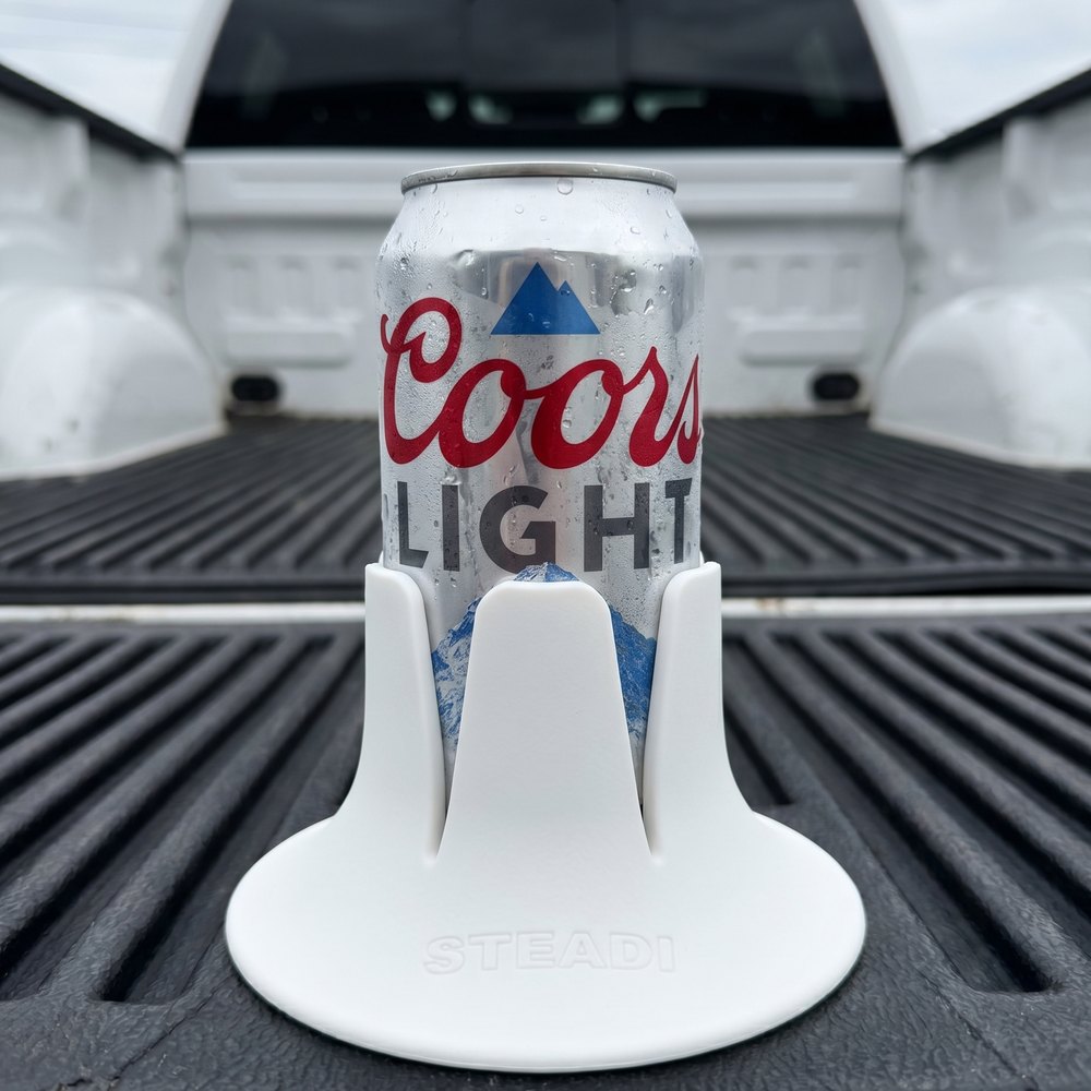 A Coors Light can standing in a white Steadi on the ribbed liner of a truck bed.
